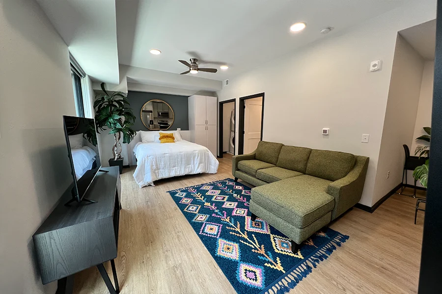 A studio apartment showing a bed and a rug under a couch